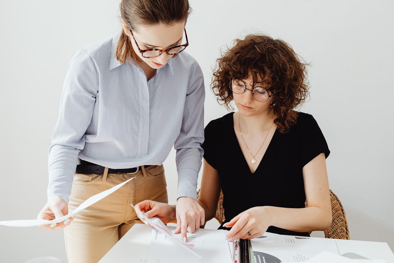 Two businesswomen reviewing documents at a workspace, focusing on collaboration and teamwork.