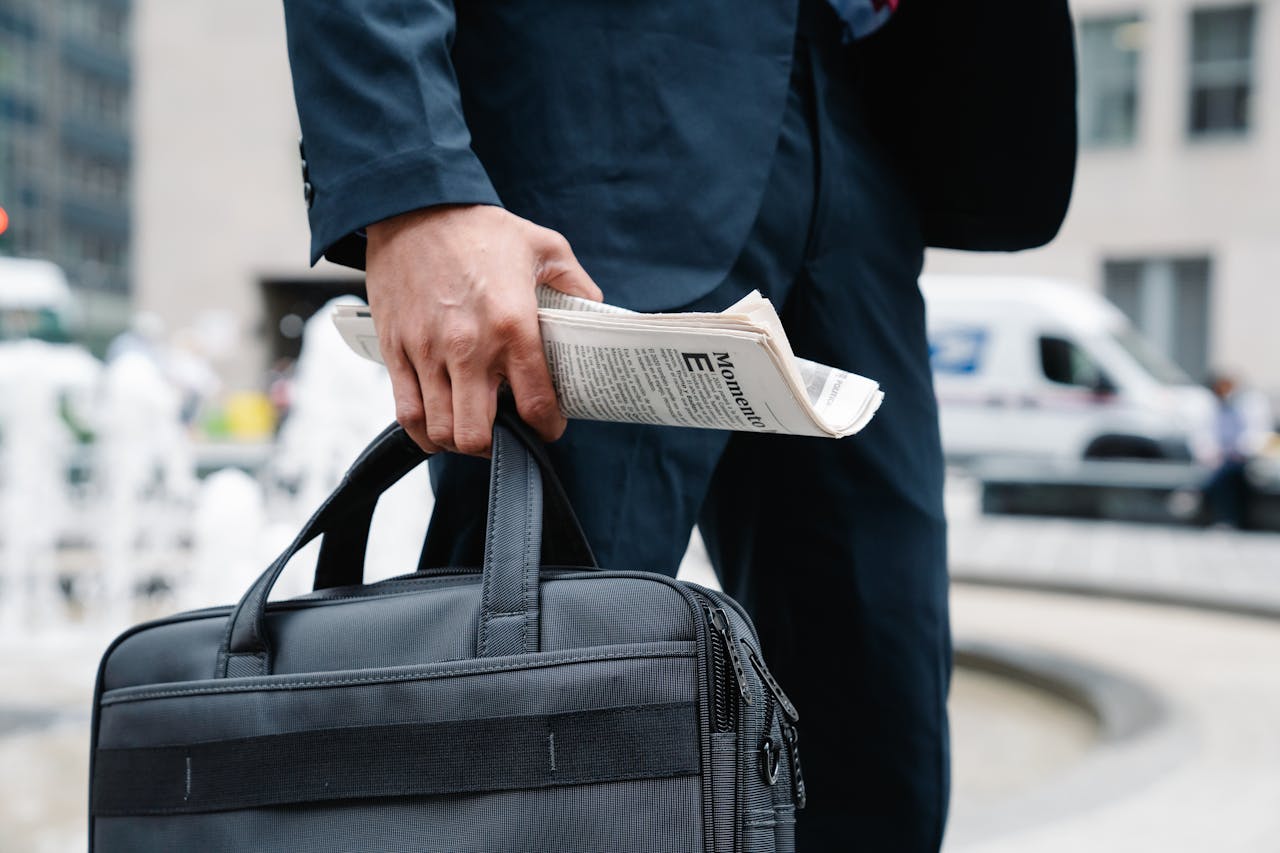 Close-up of businessman in suit holding a briefcase and newspaper in urban setting.